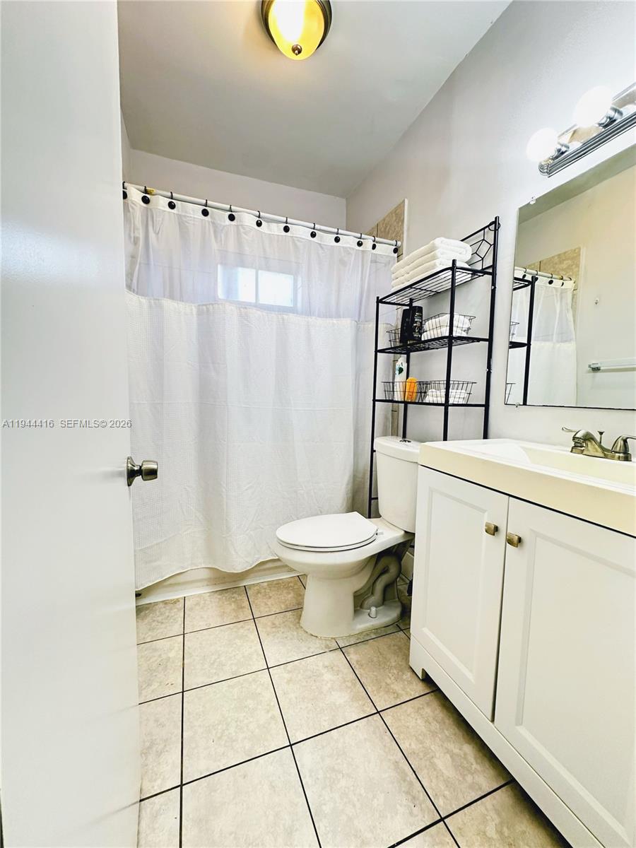 This bathroom features a white vanity, a toilet, a shower with a curtain, and shelving — 1821 NW 33rd  St, Miami FL 33142, MIAMI, FL