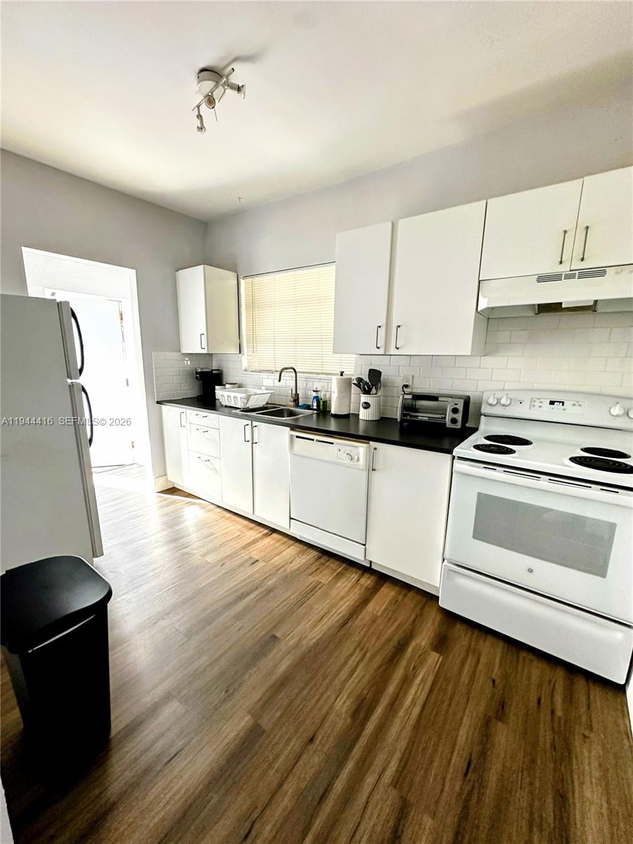 A kitchen features white cabinets, black countertops, a white stove, and wood-look flooring — 1821 NW 33rd  St, Miami FL 33142, MIAMI, FL