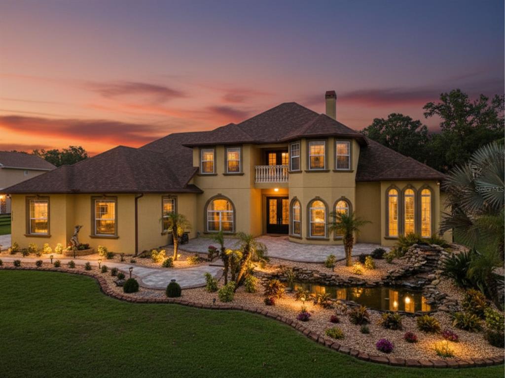A two-story stucco house with a stone patio, pond, and landscape lighting at sunset — 4524 STONE WALL LANE, PLANT CITY, FL
