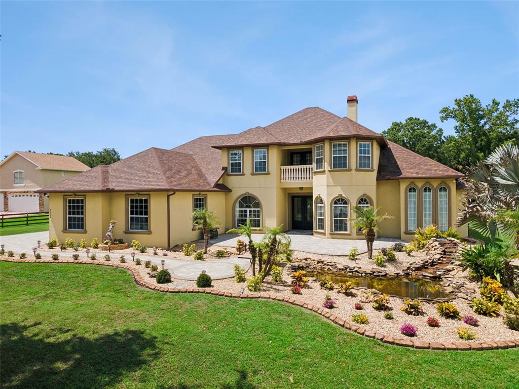 A large two-story beige house features a stone patio, a pond, and landscaped gardens — 4524 STONE WALL LANE, PLANT CITY, FL