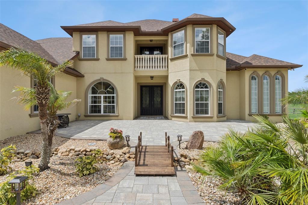 A two-story stucco house features a stone patio, a small wooden bridge, and landscaping — 4524 STONE WALL LANE, PLANT CITY, FL