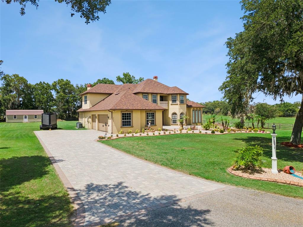 A two-story tan house with a shingled roof and paver driveway sits on a lawn — 4524 STONE WALL LANE, PLANT CITY, FL