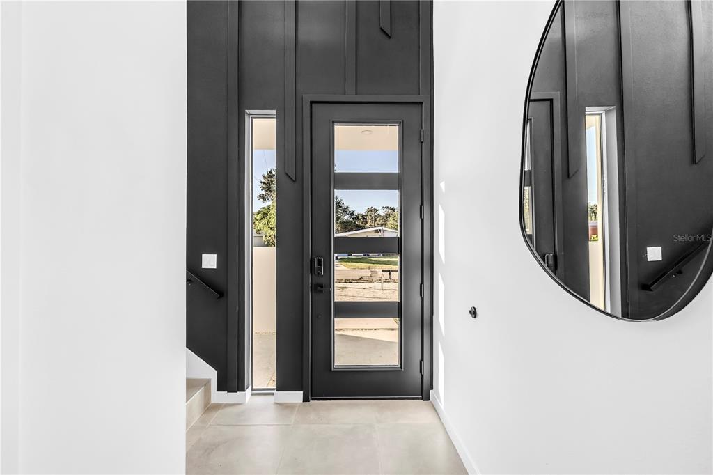 A modern entryway features a dark-framed glass door, vertical wall paneling, and a round mirror — 2305 TEMPLE STREET, SARASOTA, FL