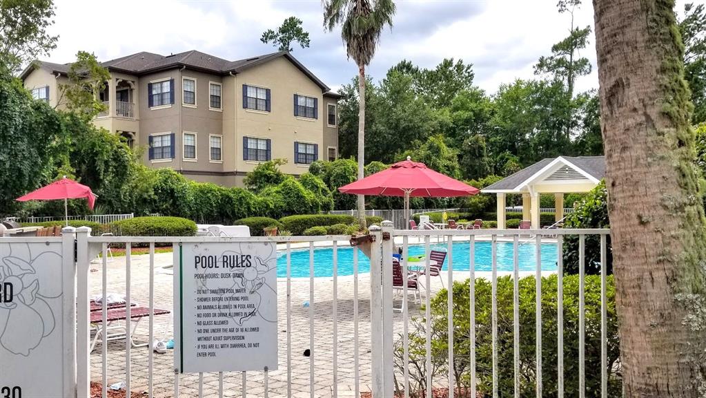 A swimming pool with red umbrellas is surrounded by a fence and apartment buildings — 4335 NW 48TH STREET UNIT 105, GAINESVILLE, FL