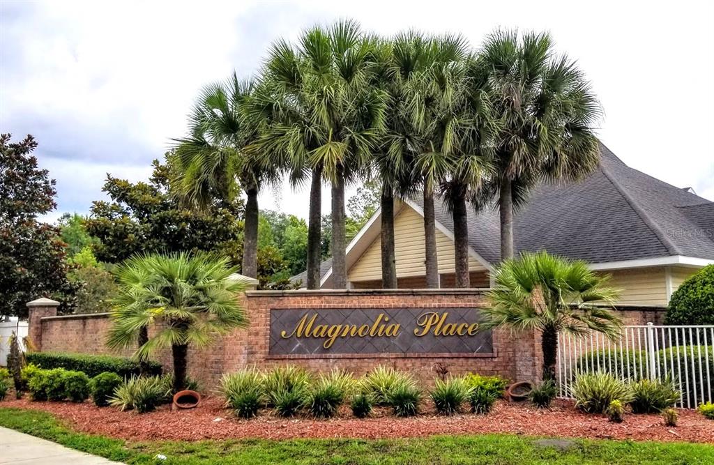 A brick entrance sign for Magnolia Place stands in front of palm trees and a building — 4335 NW 48TH STREET UNIT 105, GAINESVILLE, FL