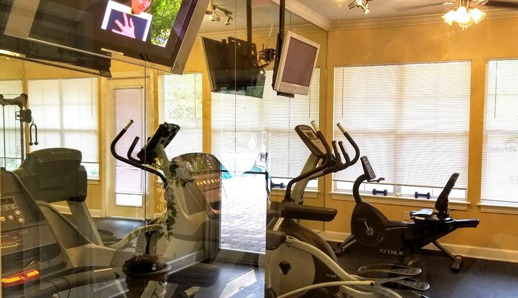 A fitness room features exercise equipment, mirrored walls, and windows with white blinds — 4335 NW 48TH STREET UNIT 105, GAINESVILLE, FL
