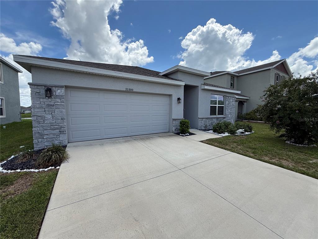 A single-story house features a two-car garage, stone veneer accents, and a concrete driveway — 31800 OYSTER TRELLIS LANE, WESLEY CHAPEL, FL