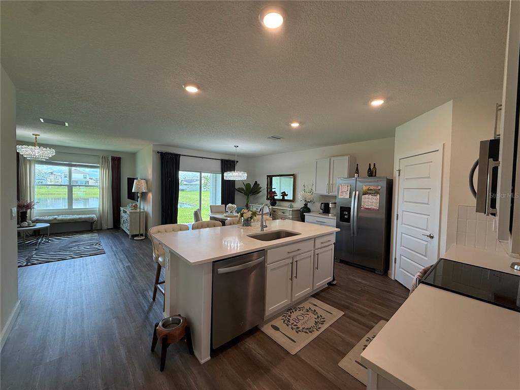 A modern kitchen with a white island and stainless steel appliances opens into a living area — 31800 OYSTER TRELLIS LANE, WESLEY CHAPEL, FL
