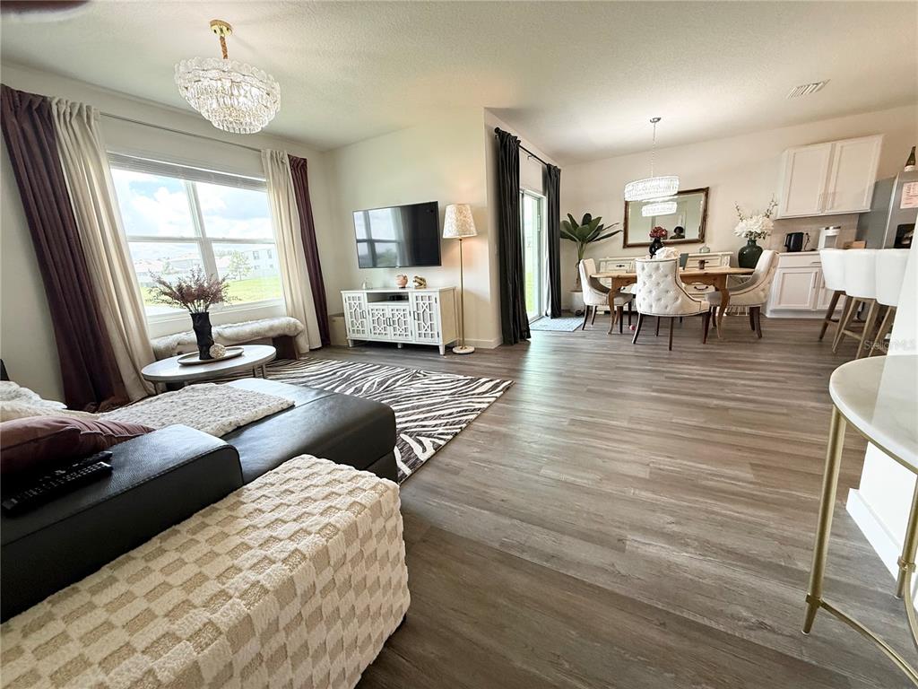 An open-concept living and dining area features wood-look flooring, neutral walls, and modern light fixtures — 31800 OYSTER TRELLIS LANE, WESLEY CHAPEL, FL
