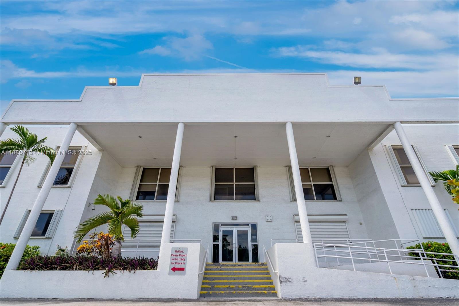 A low-angle exterior view of a white two-story building with a covered entrance and stairs — 12800 NW 38th Ave, Opa-Locka FL 33054, OPA-LOCKA, FL