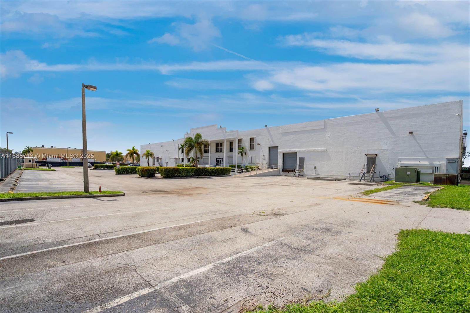 A large white industrial warehouse building features a paved parking lot and palm trees — 12800 NW 38th Ave, Opa-Locka FL 33054, OPA-LOCKA, FL