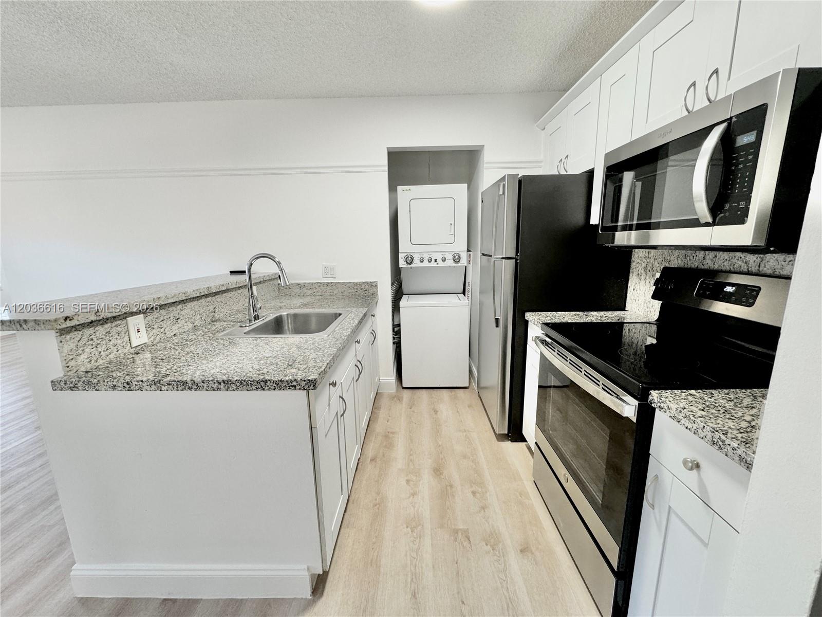 A kitchen features white cabinets, granite countertops, stainless steel appliances, and a stacked laundry unit — 4581 W Mcnab Rd # 12, Pompano Beach FL 33069, POMPANO BEACH, FL