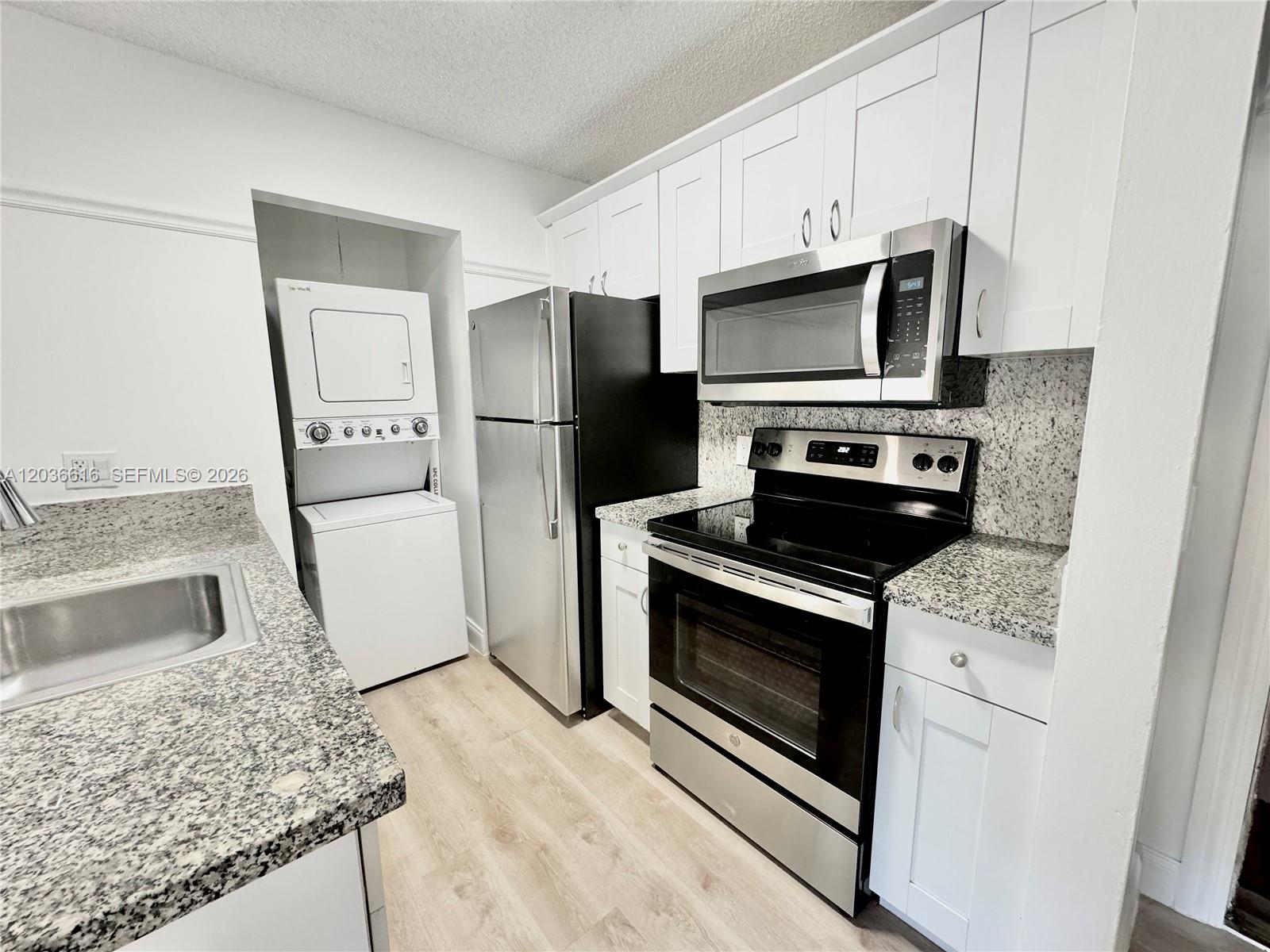 A kitchen features white cabinetry, granite countertops, stainless steel appliances, and a stacked laundry unit — 4581 W Mcnab Rd # 12, Pompano Beach FL 33069, POMPANO BEACH, FL