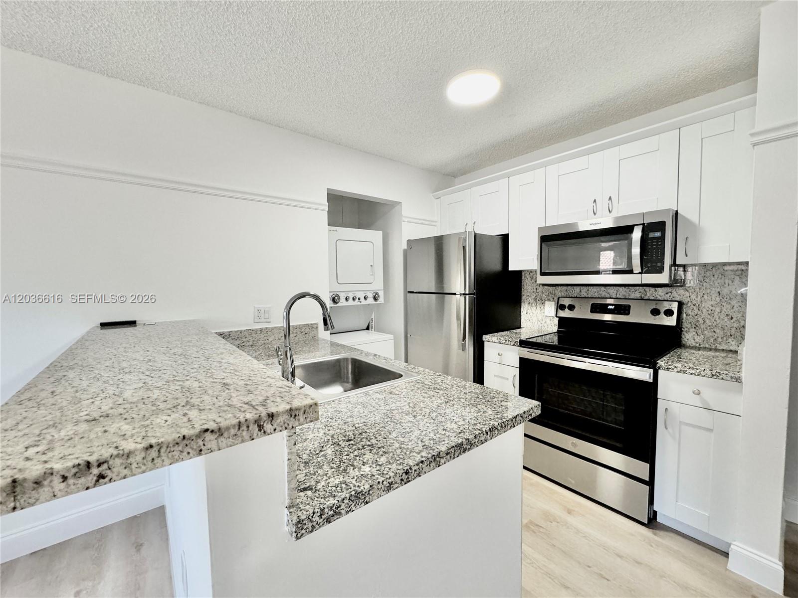 A kitchen features white cabinets, granite countertops, stainless steel appliances, and an integrated laundry closet — 4581 W Mcnab Rd # 12, Pompano Beach FL 33069, POMPANO BEACH, FL