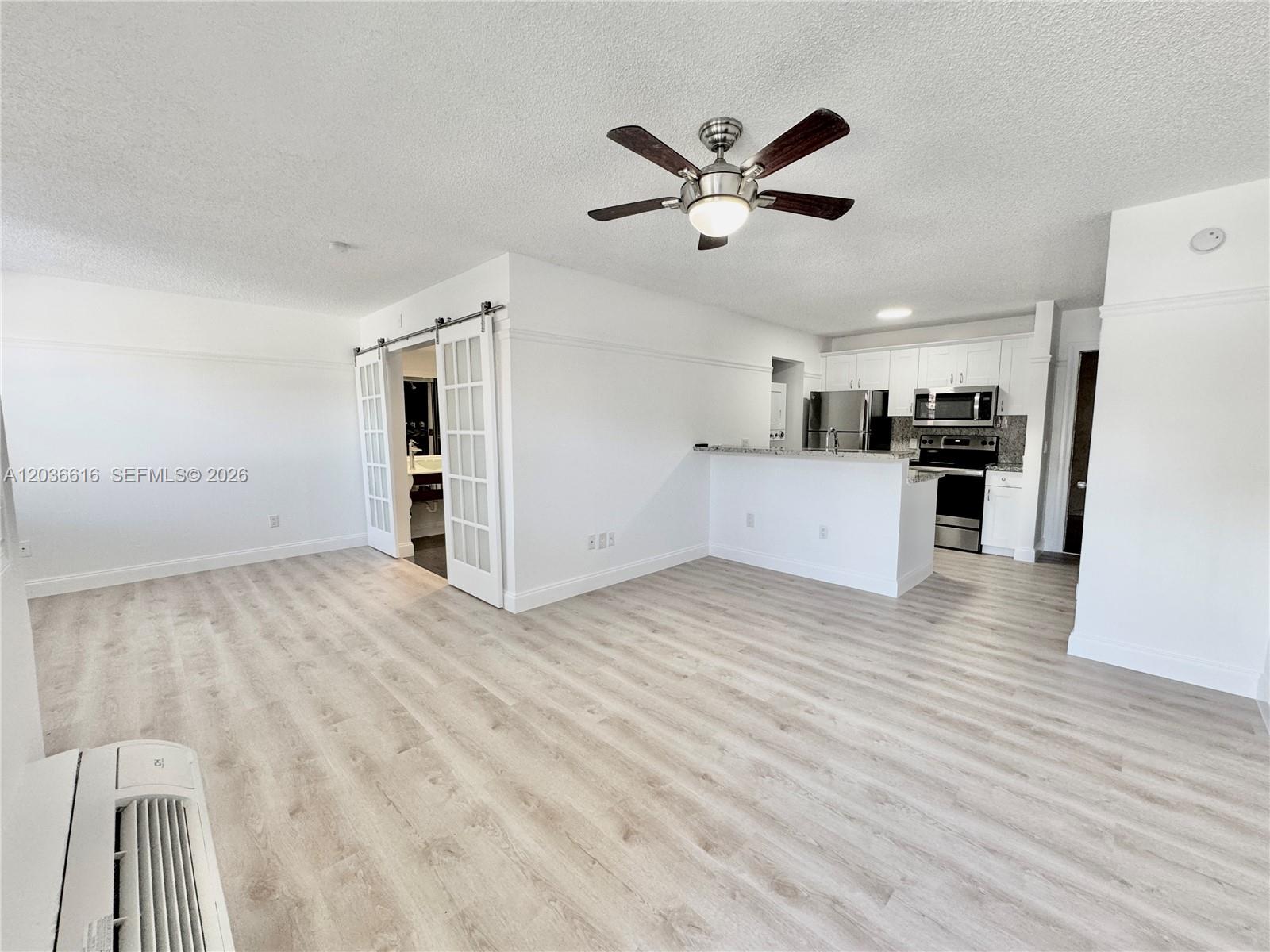 An open-concept living area features light wood-look flooring, a ceiling fan, and a kitchen — 4581 W Mcnab Rd # 12, Pompano Beach FL 33069, POMPANO BEACH, FL