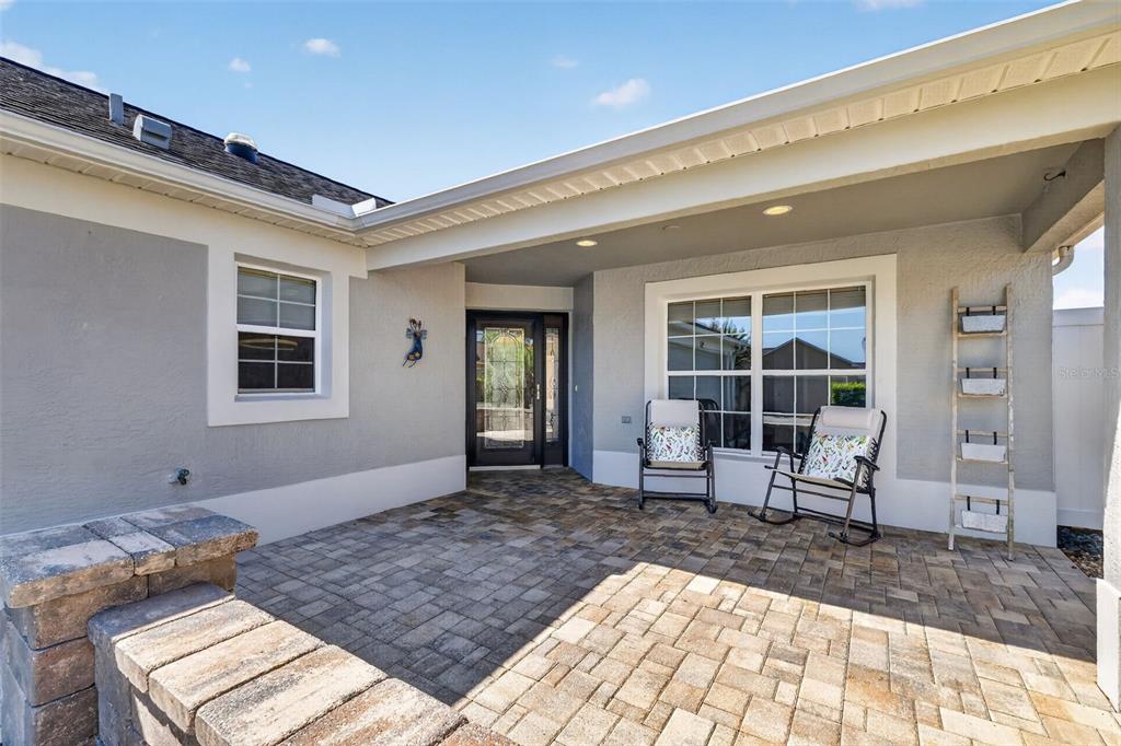 A paved patio features two rocking chairs and a decorative ladder against a house exterior — 562 AVECILLA DRIVE, THE VILLAGES, FL