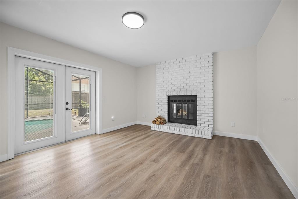 A living room with light wood-look flooring, a white brick fireplace, and glass patio doors — 2911 GRAYTON STREET, DELTONA, FL