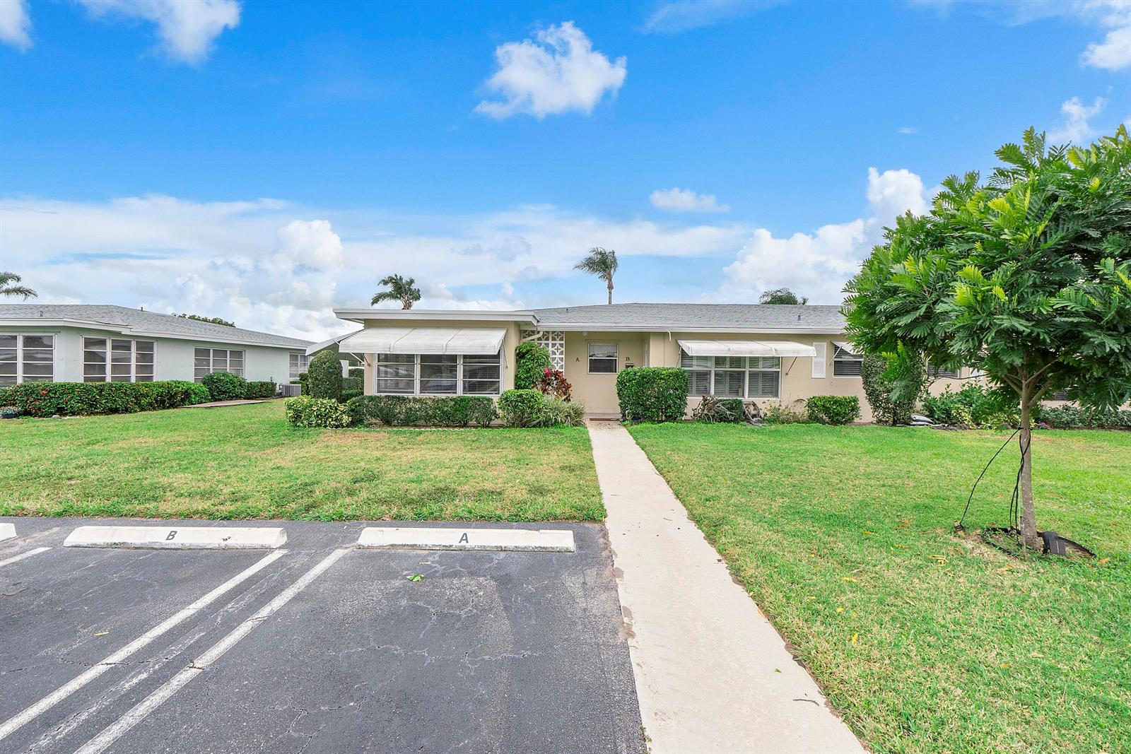 A single-story duplex with a lawn, parking spaces, and white awnings under a blue sky — 212 High Point Terrace W # A, Delray Beach FL 33445, DELRAY BEACH, FL