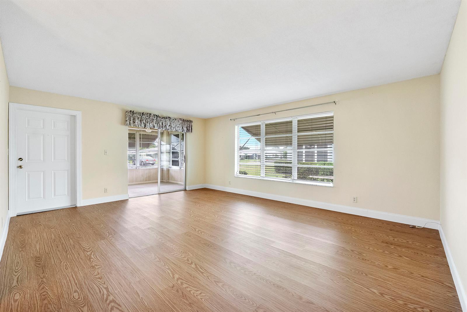 An empty living room features light-colored walls, wood-look flooring, a sliding glass door, and windows — 212 High Point Terrace W # A, Delray Beach FL 33445, DELRAY BEACH, FL