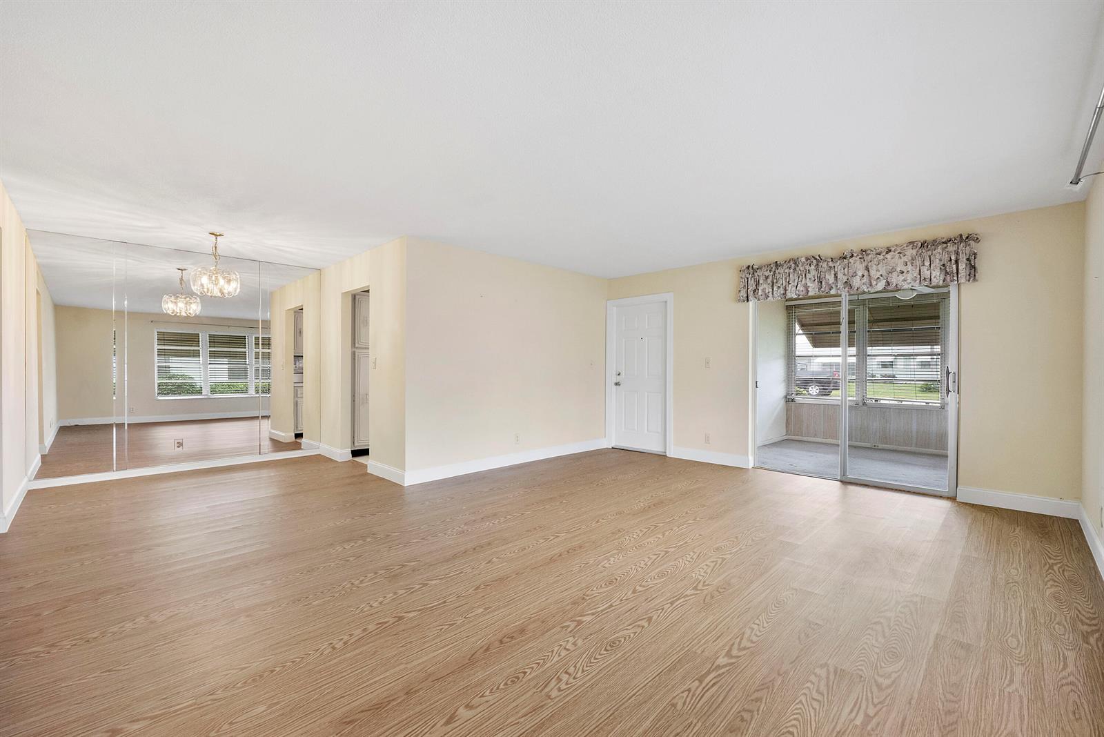 A living room with light wood-look flooring, mirrored walls, and a sliding glass door — 212 High Point Terrace W # A, Delray Beach FL 33445, DELRAY BEACH, FL
