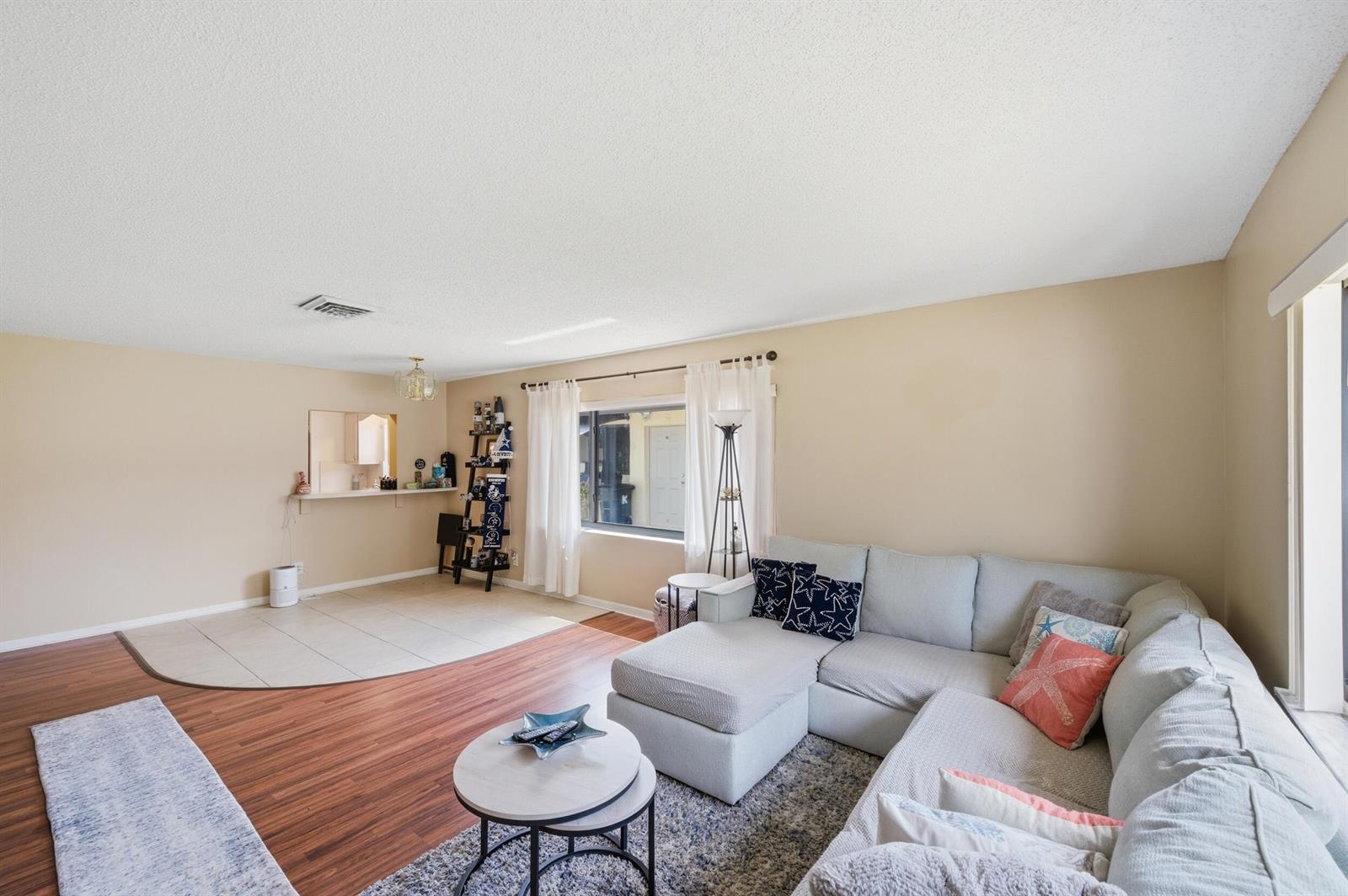 A living room with wood-look flooring, a tiled dining area, and a light-colored sectional sofa — 10222 Pine Drive, Boynton Beach FL 33437, BOYNTON BEACH, FL