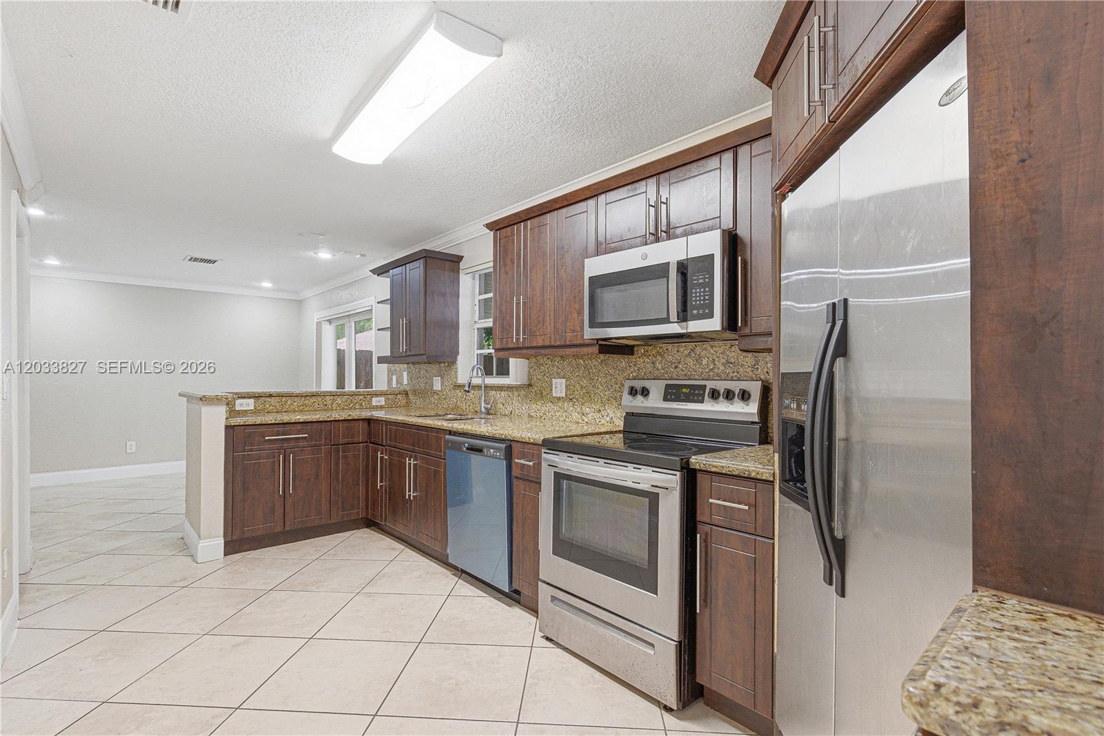 A kitchen features dark wood cabinets, granite countertops, stainless steel appliances, and tiled flooring — 9121 SW 215th Ter, Cutler Bay FL 33189, CUTLER BAY, FL