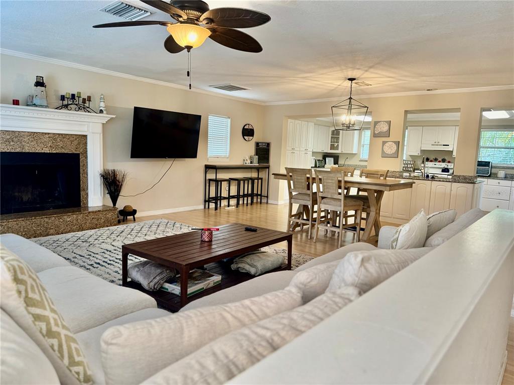 An open-concept living and dining area features a fireplace, ceiling fan, and hardwood floors — 419 KENTUCKY AVENUE, CRYSTAL BEACH, FL