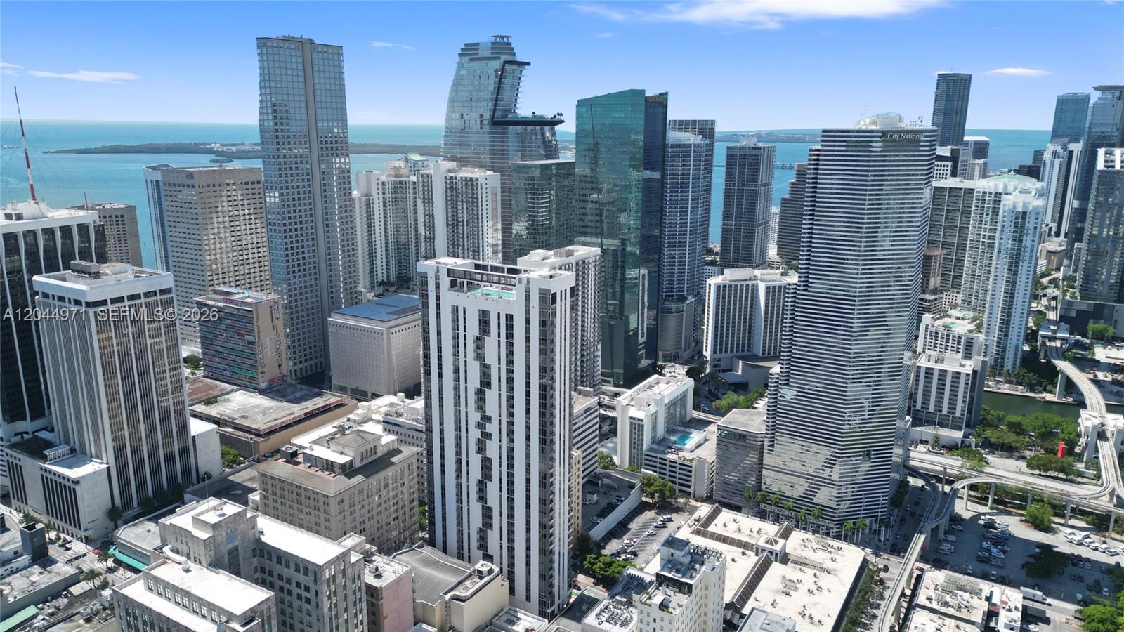 An aerial view shows a dense cityscape of high-rise buildings overlooking the ocean — 151 SE 1st St, Miami FL 33131, MIAMI, FL