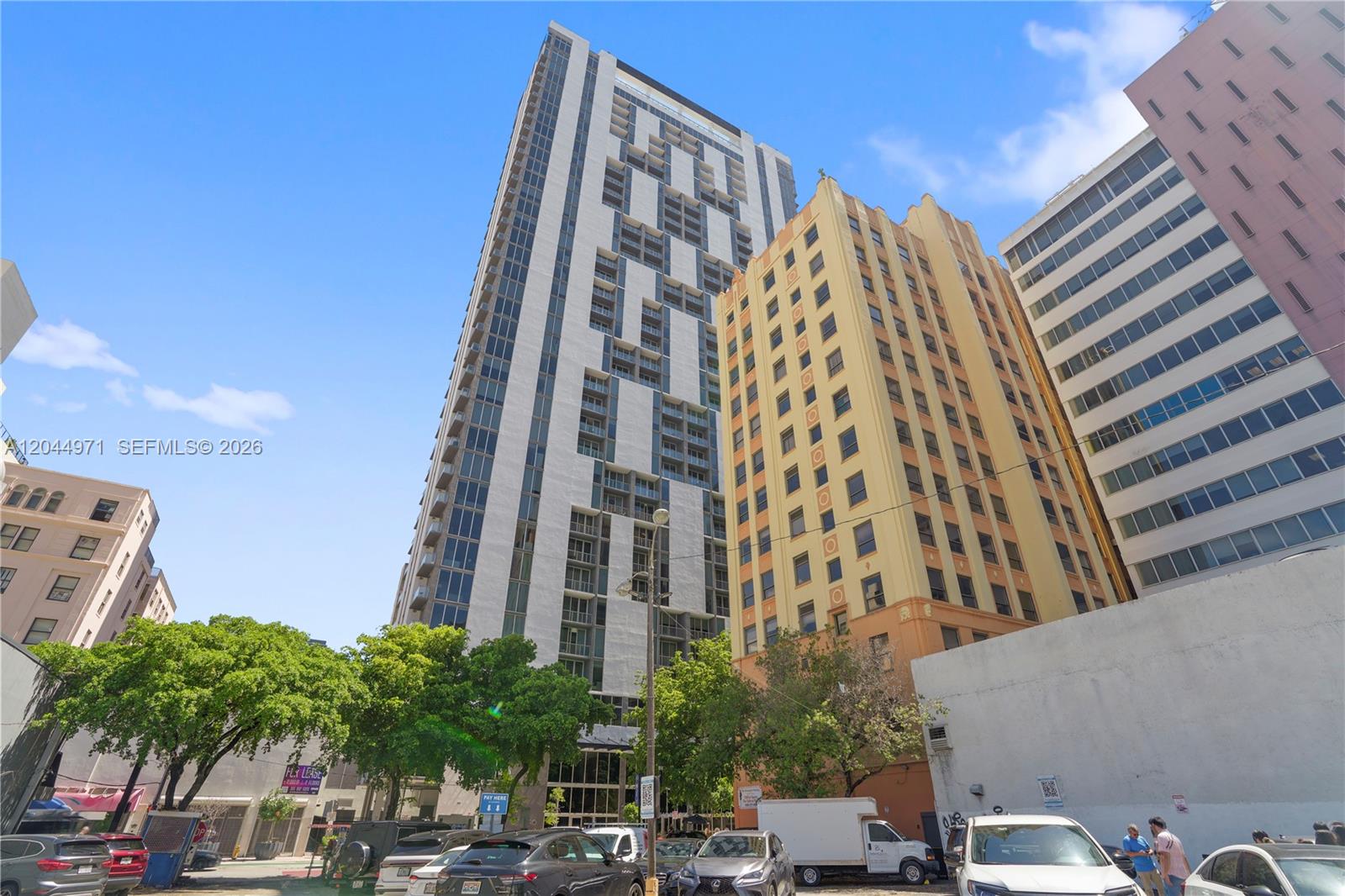 A low-angle view shows a modern white high-rise building next to a historic yellow building — 151 SE 1st St, Miami FL 33131, MIAMI, FL
