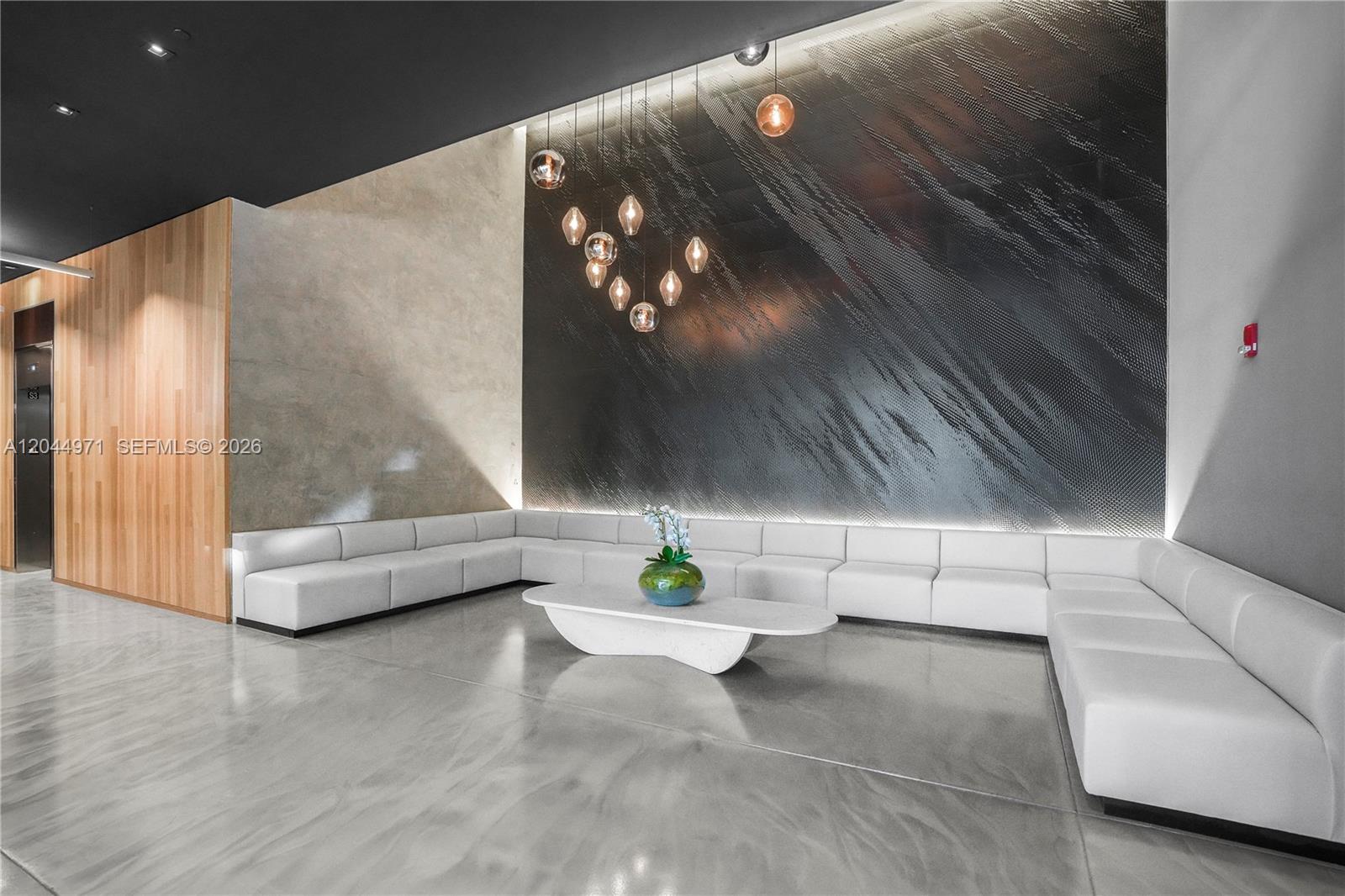 A modern lobby features a large white sectional sofa, a coffee table, and textured walls — 151 SE 1st St, Miami FL 33131, MIAMI, FL