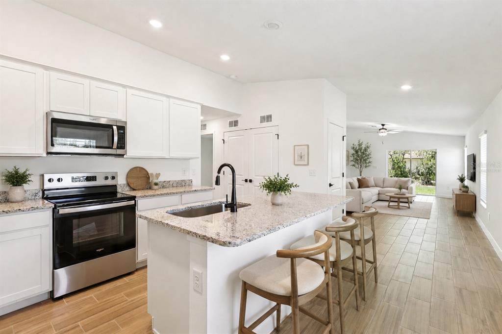 A kitchen with white cabinets, granite countertops, and an island opens to a living room — 614 BLACKTHORN DRIVE, LAKELAND, FL
