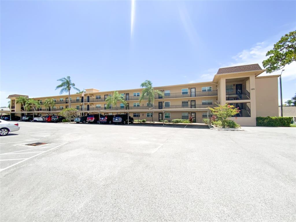 A multi-story apartment building with a large parking lot and covered parking spaces — 1370 HEATHER RIDGE BOULEVARD UNIT 204, DUNEDIN, FL