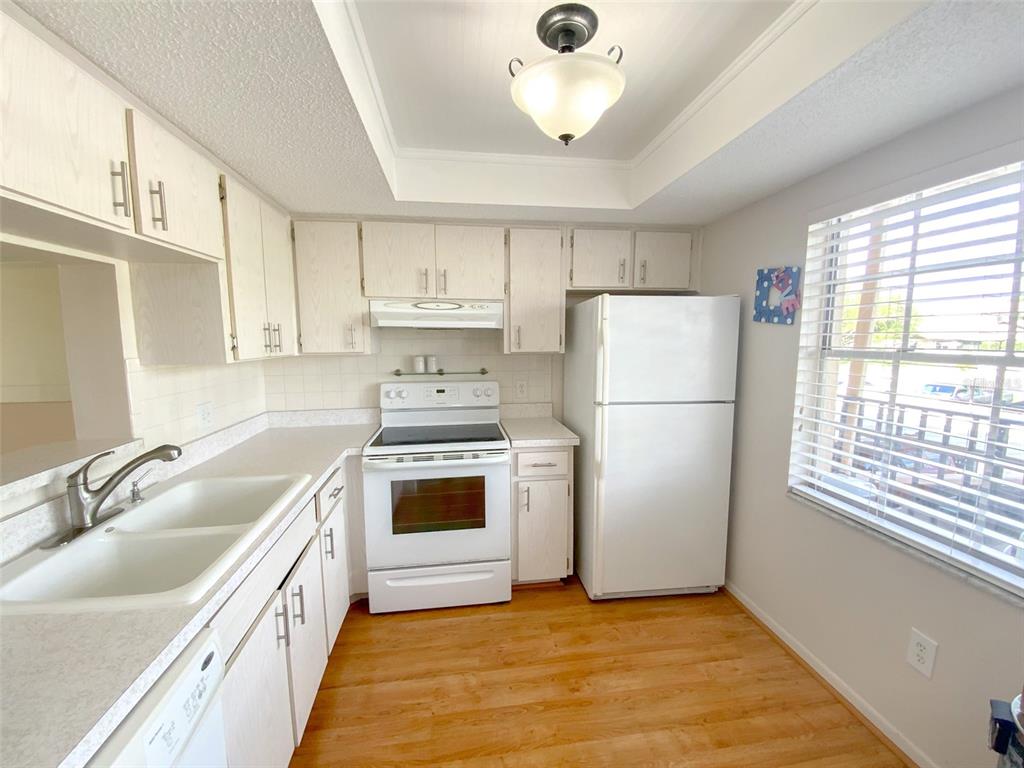 A kitchen features white cabinets, white appliances, a double sink, and light wood flooring — 1370 HEATHER RIDGE BOULEVARD UNIT 204, DUNEDIN, FL