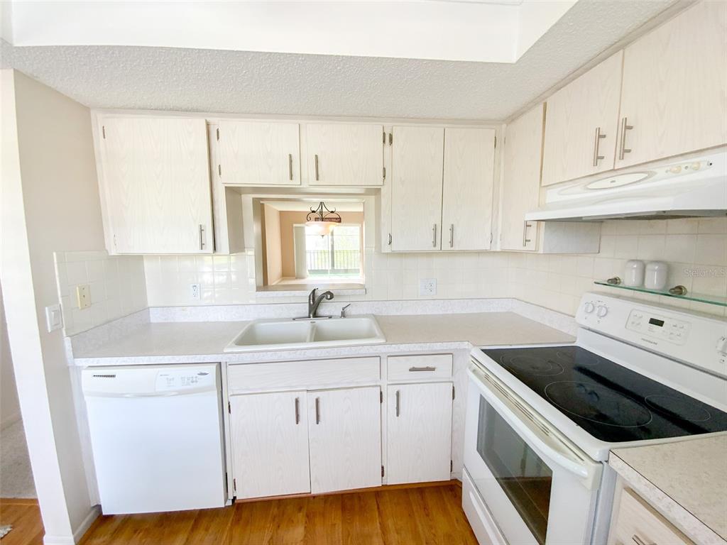 A kitchen features white cabinets, laminate countertops, a double sink, and white appliances — 1370 HEATHER RIDGE BOULEVARD UNIT 204, DUNEDIN, FL