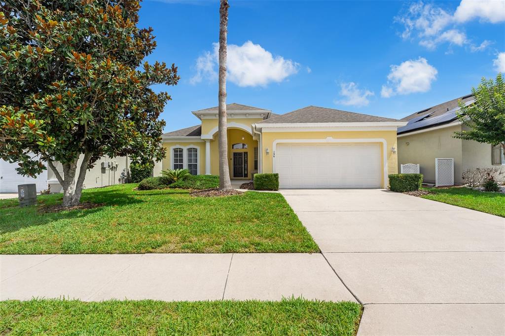 A yellow single-story house with a two-car garage and a palm tree in the front yard — 196 MINNIEHAHA CIRCLE, HAINES CITY, FL