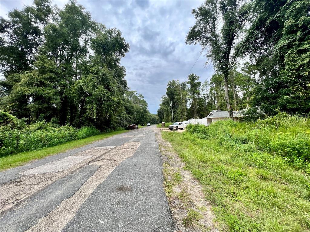 A paved road with patches leads toward trees and a house under a cloudy sky — 325 W ERIDANI COURT, CITRUS SPRINGS, FL
