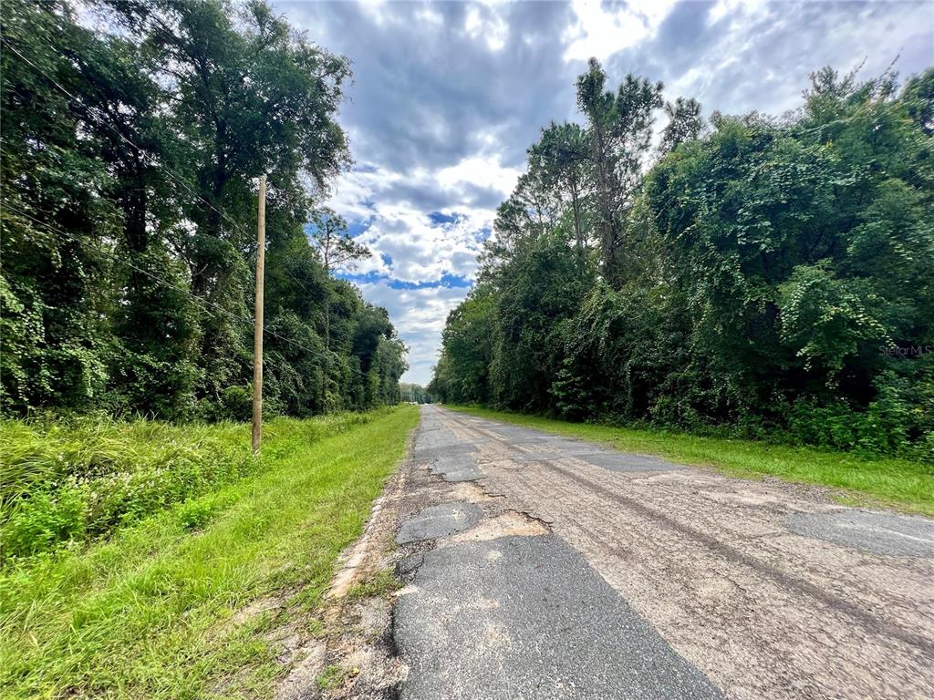A paved road with patches runs through a wooded area under a cloudy sky — 325 W ERIDANI COURT, CITRUS SPRINGS, FL