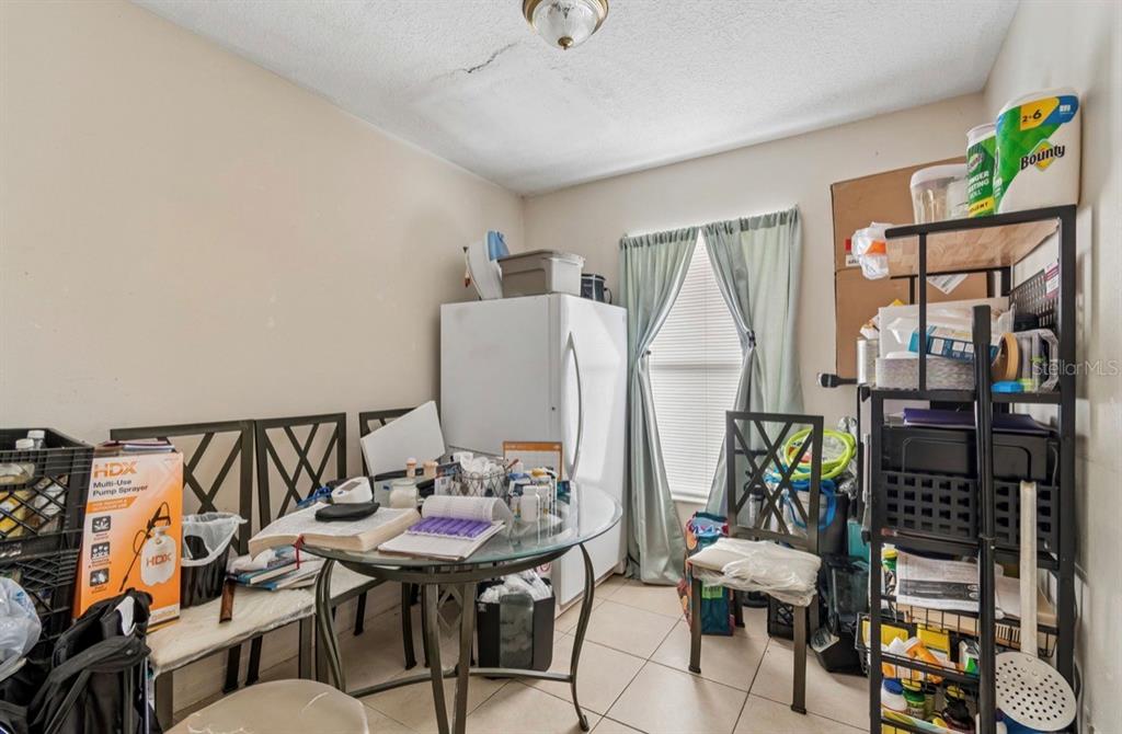A cluttered dining area with a glass table, chairs, a refrigerator, and metal shelving units — 1901 E 32ND AVENUE, TAMPA, FL