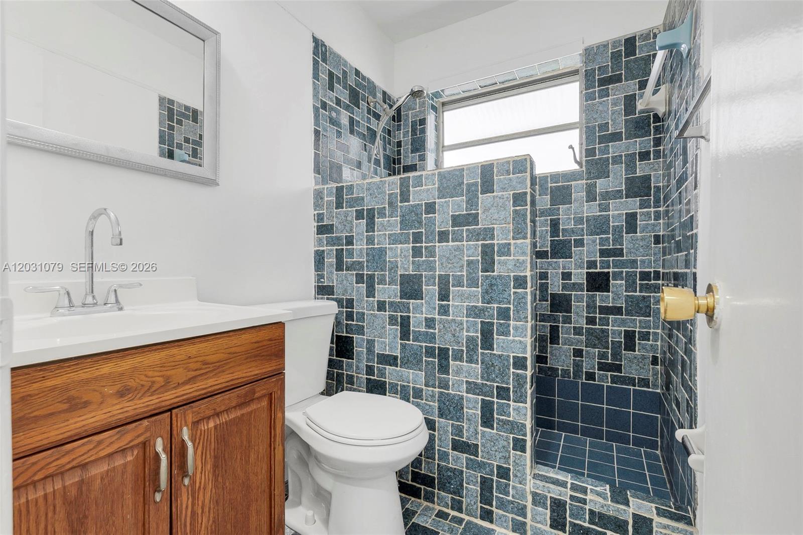 A bathroom features a wood vanity, white toilet, and a shower with blue mosaic tiles — 6101 SW 24th St # 3, Miramar FL 33023, MIRAMAR, FL