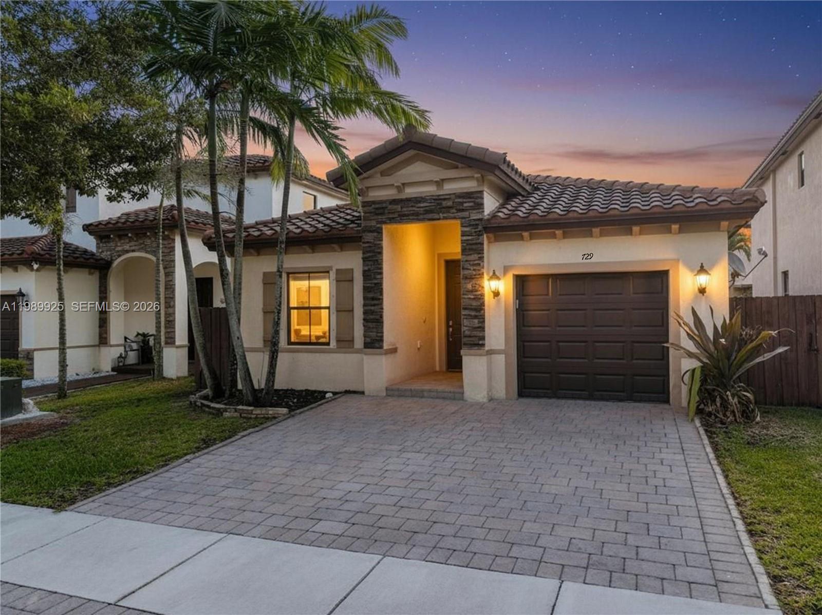 A single-story house with a tiled roof, stone accents, and a paved driveway at dusk — 729 SE 34th Ave, Homestead FL 33033, HOMESTEAD, FL