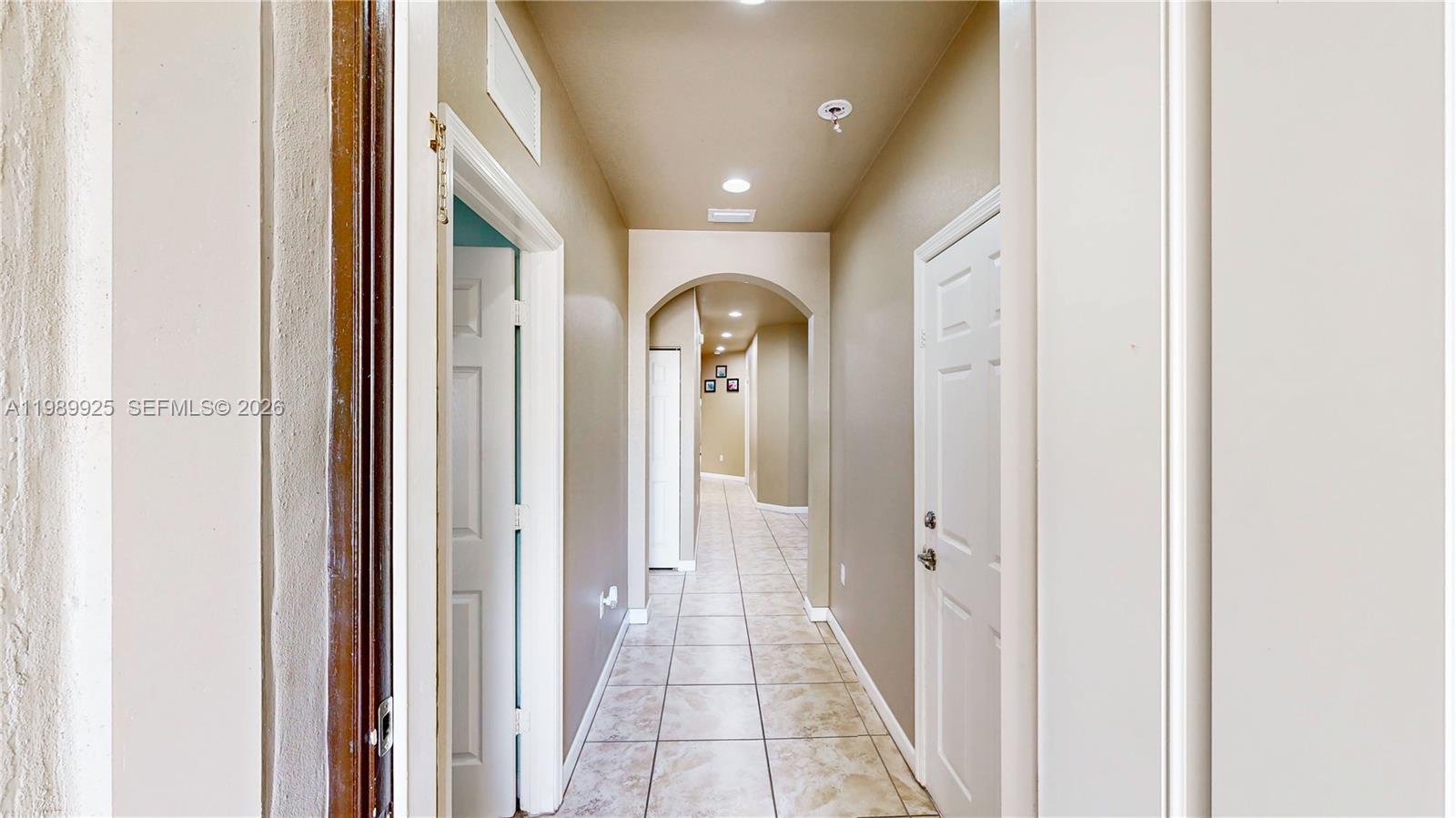 A tiled hallway features arched transitions, beige walls, and white doors — 729 SE 34th Ave, Homestead FL 33033, HOMESTEAD, FL