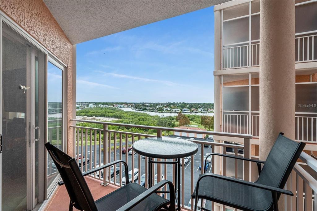 A balcony with a small table and two chairs overlooks a parking lot and waterway — 4516 SEAGULL DRIVE UNIT 614, NEW PORT RICHEY, FL