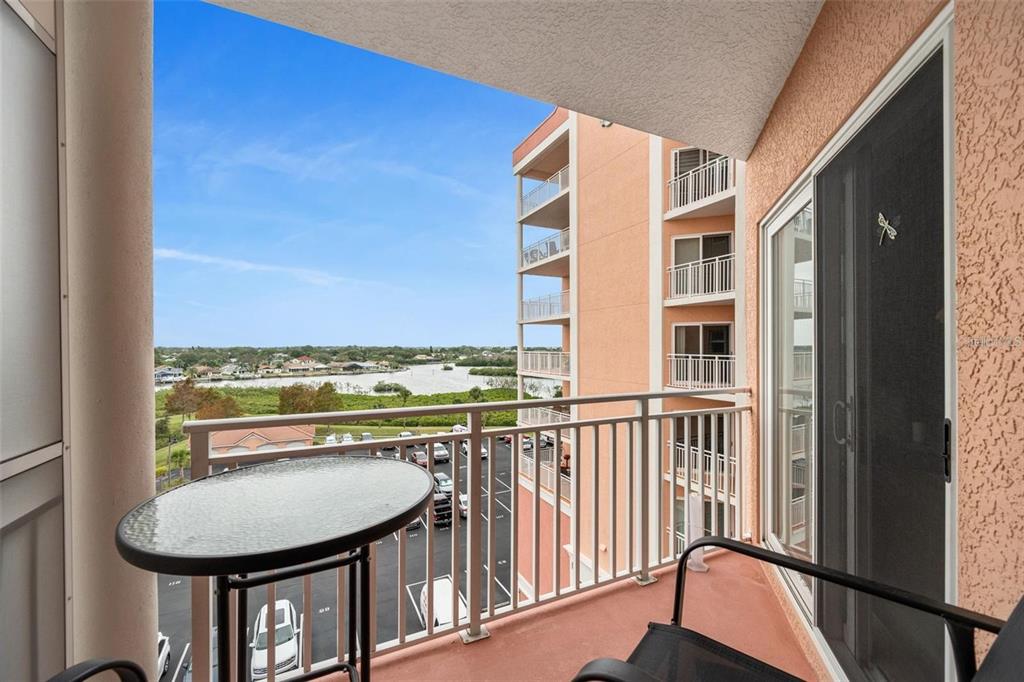 A balcony with a glass-topped table and chairs overlooks a parking lot and water — 4516 SEAGULL DRIVE UNIT 614, NEW PORT RICHEY, FL