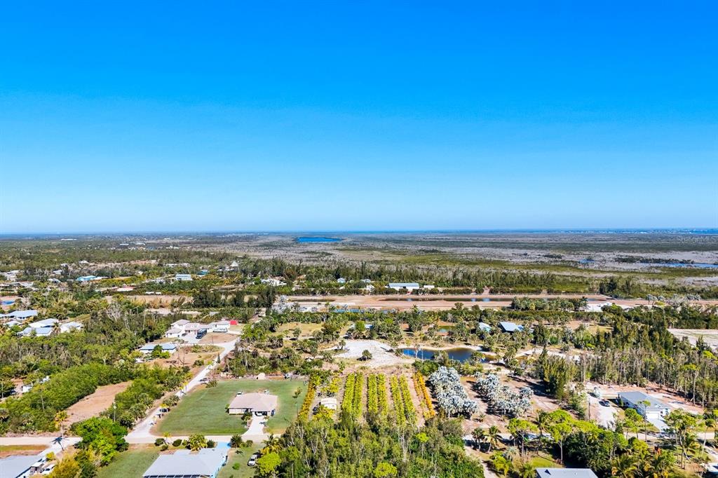 An aerial view shows a rural landscape with scattered houses, vegetation, and a distant coastline — 4442 COURTNEY ROAD, ST JAMES CITY, FL