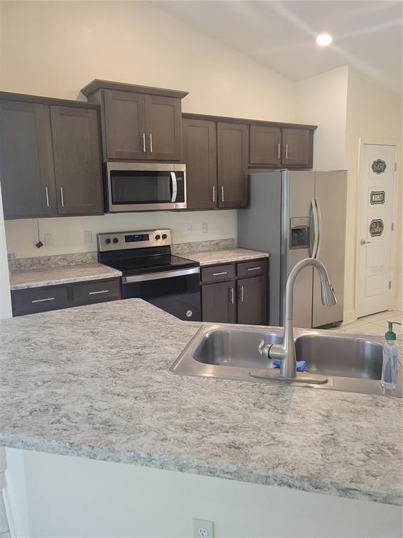 A kitchen features dark wood cabinets, stainless steel appliances, and a light-colored stone countertop — 25 BARRINGTON DRIVE, PALM COAST, FL