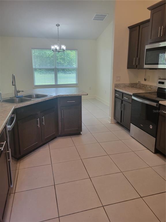 A kitchen features dark wood cabinets, stainless steel appliances, and light-colored tile flooring — 25 BARRINGTON DRIVE, PALM COAST, FL