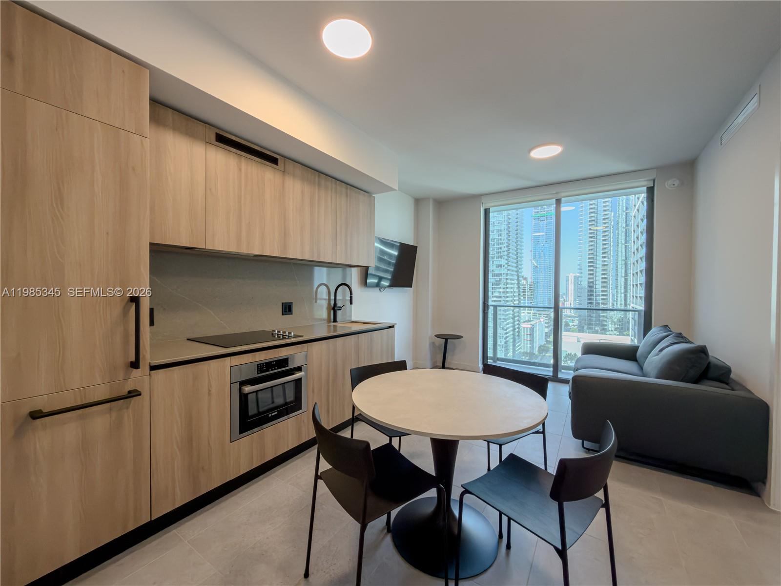 A modern studio apartment features a kitchenette, a dining table, and a gray sofa — 121 NE 5th St # 2211, Miami FL 33132, MIAMI, FL