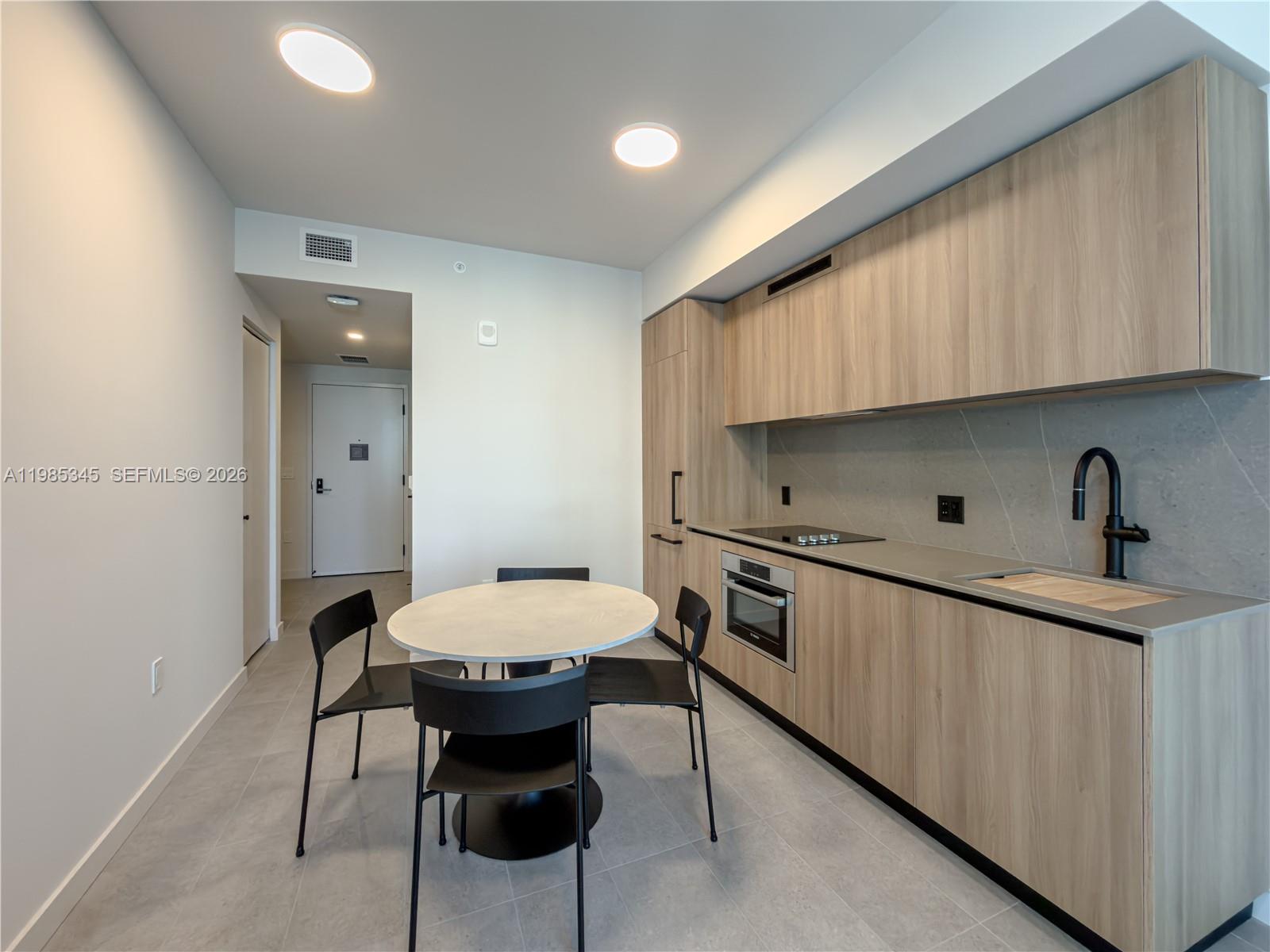 A modern kitchen features light wood cabinetry, a round dining table, and gray tile flooring — 121 NE 5th St # 2211, Miami FL 33132, MIAMI, FL