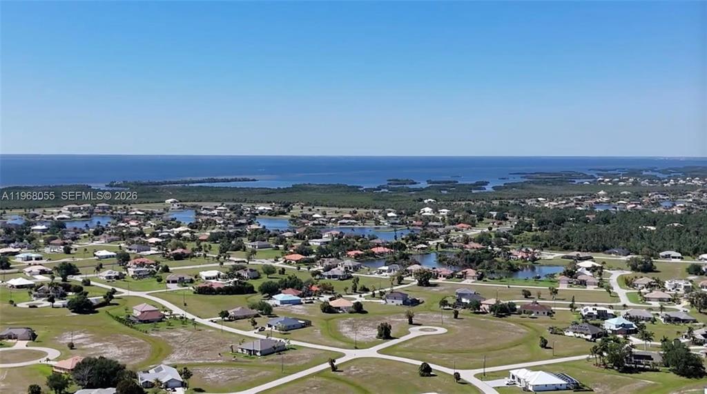 An aerial view shows a residential neighborhood with houses, ponds, and a distant coastline — 17285 ACAPULCO ROAD, PUNTA GORDA, FL