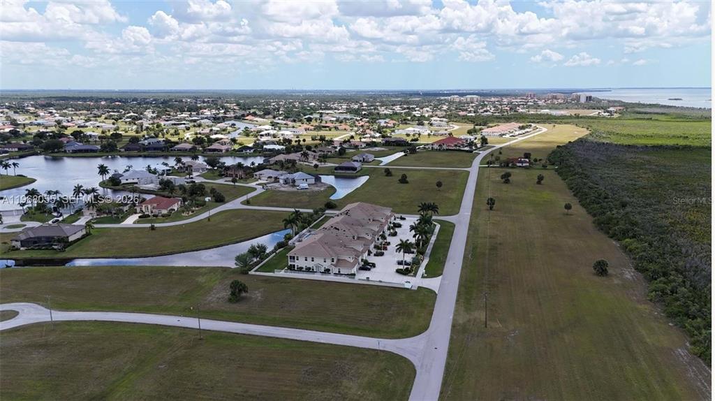 An aerial view shows a multi-unit residential building surrounded by suburban homes and undeveloped land — 17285 ACAPULCO ROAD, PUNTA GORDA, FL